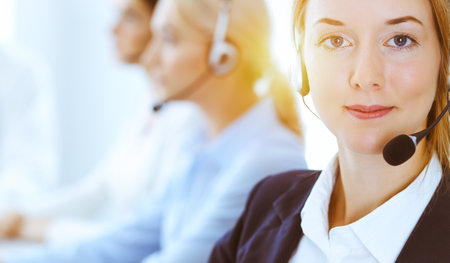 Group of diverse phone operators at work in sunny office. Handsome business woman with headphones consulting clients. Call center and business people conceptの写真素材