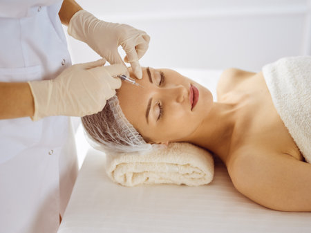 Beautiful woman receiving beauty injections with closed eyes. Beautician doctor hands doing beauty procedure to female face with syringe. Cosmetic medicine and surgery conceptの写真素材
