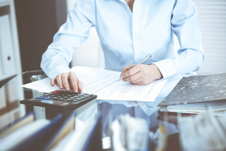 Bookkeeper woman or financial inspector making report, calculating or checking balance, close-up. Business, audit or tax concepts.の写真素材
