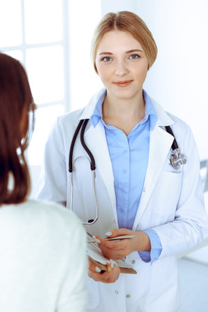 Young woman doctor and patient at medical examination at hospital office. Blue color blouse of therapist looks good. Medicine and healthcare conceptの写真素材