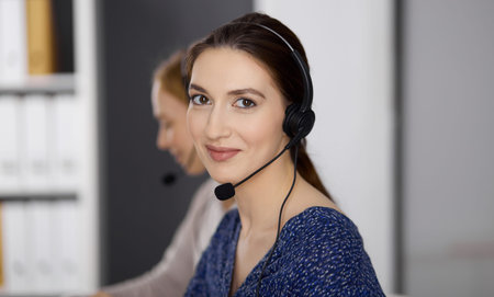 Latin american businesswoman talking by headset while sitting in office. Call center and diverse...