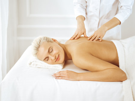 Beautiful blonde woman enjoying back massage with closed eyes. Spa salon conceptの写真素材