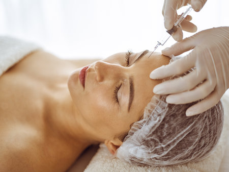 Beautician doing beauty procedure with syringe to face of young brunette woman. Cosmetic medicine and surgery, beauty injections.の写真素材