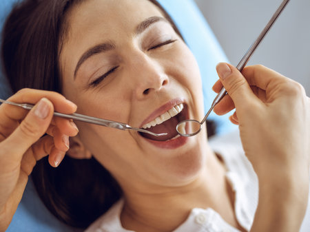 Smiling brunette woman being examined by dentist at dental clinic. Hands of a doctor holding dental instruments near patients mouth. Healthy teeth and medicine conceptの写真素材