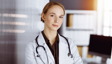 Cheerful smiling female doctor standing with arms crossed in clinic. Portrait of friendly physician woman. Medicine conceptの写真素材