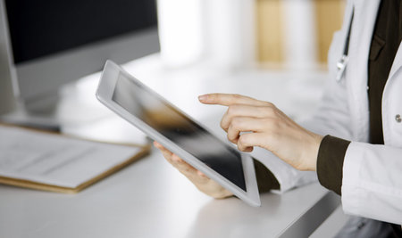 Unknown female doctor using tablet computer in clinic. Perfect medical service in hospital. Medicine...