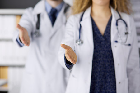 Two doctors standing and offering helping hand for shaking hand or saving life. Medical help, countering viral infection and medicine conceptの写真素材