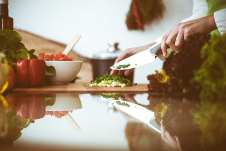 Unknown human hands cooking in kitchen. Woman slicing green onion. Healthy meal, and vegetarian food concept.の写真素材