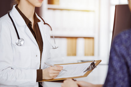 Doctor and patient discussing current health examination while sitting in sunny clinic. Perfect medical service in hospitalの写真素材