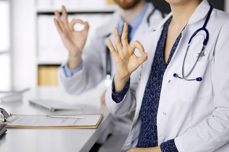 Two doctors sitting with Ok sign in hospital office. Medical help, countering viral infection and medicine conceptの写真素材