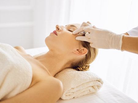 Beautiful woman receiving beauty injections with closed eyes. Beautician doctor hands doing beauty procedure to female face with syringe. Cosmetic medicine and surgery conceptの写真素材