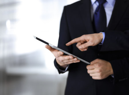 Business people using a tablet computer, while working together in a modern office. Unknown businessman or male entrepreneur with a colleague at workplace. Teamwork and partnership concept.の写真素材