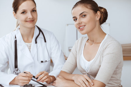 Doctor and patient are sitting and discussing health examination results in clinic office. Health care, medicine and good news conceptsの写真素材