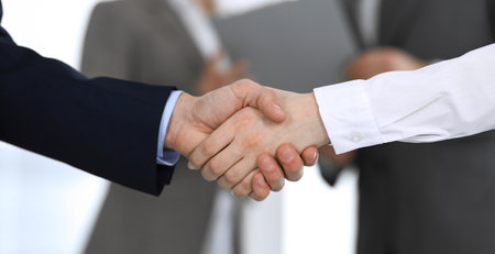 Business people shaking hands while standing with colleagues after meeting or negotiation, close-up. Group of unknown businessmen and women in modern office. Teamwork, partnership and handshake concept, toned picture.の写真素材