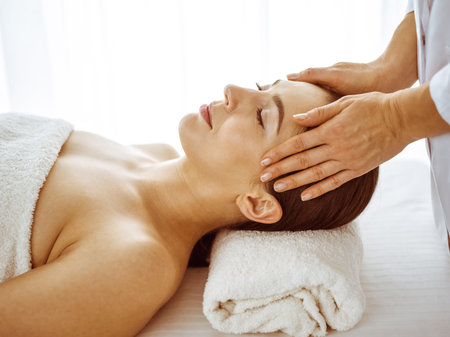Beautiful brunette woman enjoying facial massage with closed eyes. Relaxing treatment in medicine and spa center conceptsの写真素材