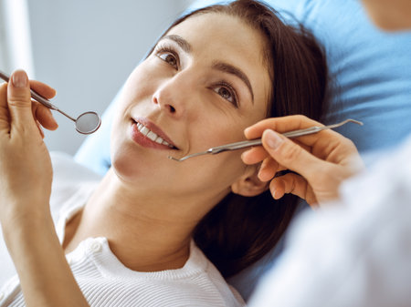 Smiling brunette woman being examined by dentist at dental clinic. Hands of a doctor holding dental instruments near patients mouth. Healthy teeth and medicine conceptの写真素材
