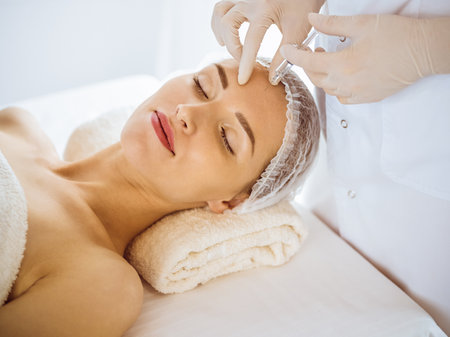 Beautiful woman receiving beauty injections with closed eyes in medical center. Beautician doctor hands doing beauty procedure to female face with syringe. Cosmetic medicine and surgery conceptの写真素材