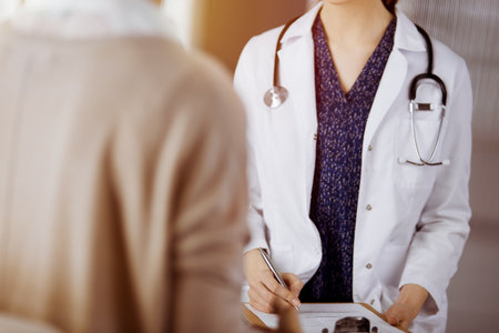 Doctor and patient discussing current health examination while sitting in sunny clinic. Perfect medical service in hospitalの写真素材