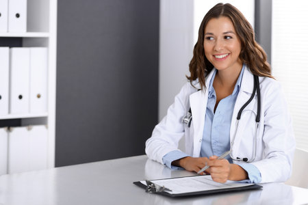 Doctor woman filling up medical form while sitting at the desk in hospital office. Physician at work. Medicine and health care conceptの写真素材