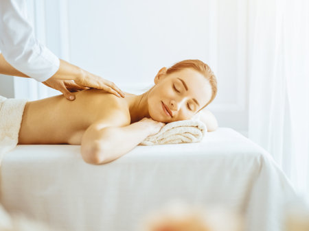 Beautiful woman enjoying back massage with closed eyes in sunny spa centerの写真素材
