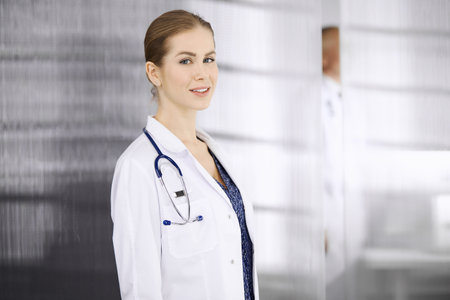 Cheerful female doctor standing in clinic. Portrait of friendly smiling woman physician. Perfect medical service in hospital. Medicine conceptの写真素材