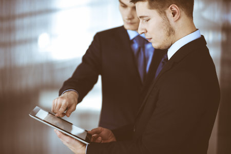 Business people, using a tablet computer, while standing in a modern office. Unknown businessman with a colleague at workplace. Teamwork and partnership conceptの写真素材