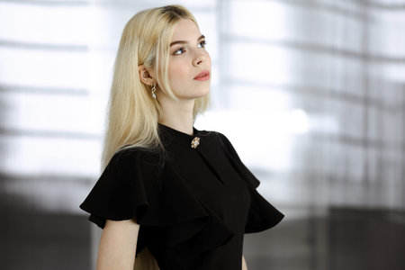 Young blonde business woman or female student in black is standing straight and posing at camera....