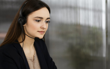 Two young people in headsets are smiling and talking to the clients, while sitting at the desk in a modern office. Call center operators at workの写真素材