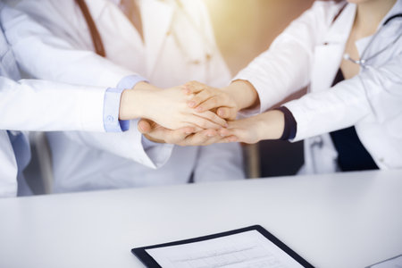 Group of doctors joining hands as a circle and ready to help patients while sitting at the desk in modern hospital office.の写真素材