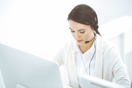 Call center. Casual dressed woman sitting and working in headset at customer service office....