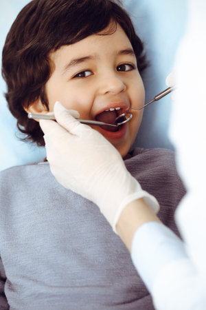 Little arab boy sitting at dental chair with open mouth during oral checking up with dentist doctor....