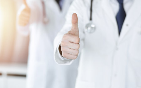 Group of unknown doctors standing as a team with thumbs up or Ok sign in hospital office, close-up. Medical help, insurance in health care, best treatment and medicine conceptの写真素材
