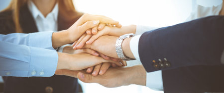 Business team showing unity with their hands together in sunny office. Group of people joining hands...