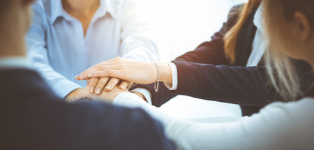 Business team showing unity with their hands together in sunny office. Group of people joining hands...