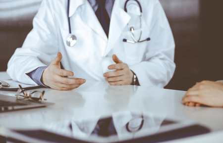 Unknown male doctor and patient woman discussing something while sitting in clinic and using clipboard. Best medical service in hospital, medicine, pandemic stopの写真素材