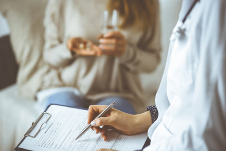 Unknown woman-doctor and patient discussing current health examination while sitting indoors. Stay at home concept during pandemic and self isolation quarantineの写真素材
