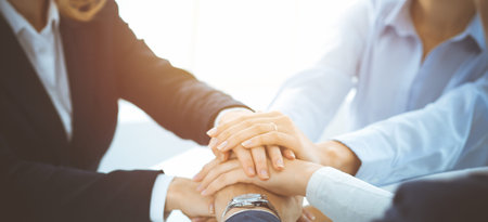 Business team showing unity with their hands together in sunny office. Group of people joining hands...