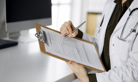 Cheerful smiling female doctor using clipboard in clinic. Portrait of friendly physician woman at work place. Perfect medical service in hospital. Medicine conceptの写真素材