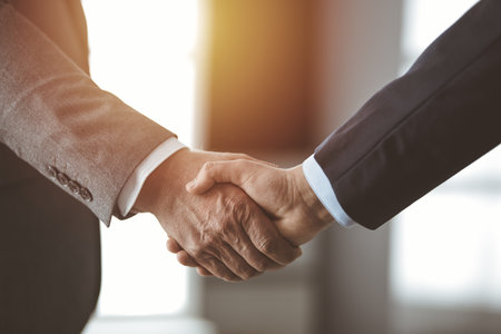 Business people standing and shaking hands in sunny office, close-up. Handshake and marketingの写真素材