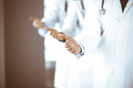 Group of unknown modern doctors stand as a team with open hands in a hospital office. Physicians ready to examine and help patients. Medical help, insurance in health care, best disease treatment and medicine concept.の写真素材