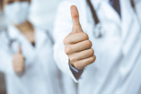 Unknown man-doctor and woman standing straight as a team and showing Ok sign with thumbs up in modern clinic. Medicine concept during Coronavirus pandemic. Covid 2019の写真素材