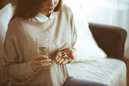 Close-up woman holding pills time to take medications, cure for headache, high blood pressure pain killer drugs at home. Stay at home concept during Coronavirus pandemicの写真素材