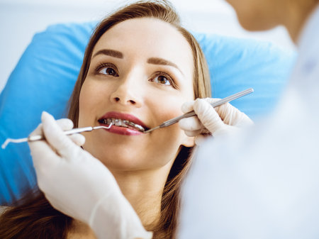 Smiling young woman with orthodontic brackets examined by dentist in dental clinic. Healthy teeth and medical care conceptの写真素材