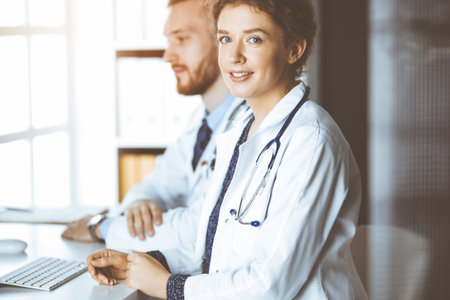 Friendly female doctor sitting in clinic with her male colleague at the background in sunny clinic. Medicine conceptの写真素材