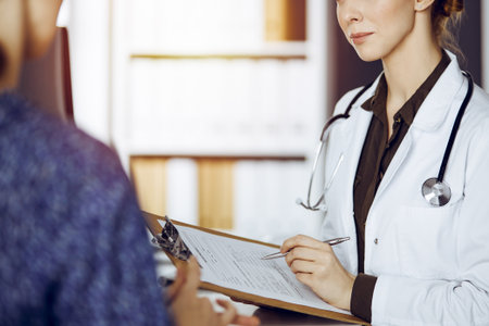 Doctor and patient discussing current health examination while sitting in sunny clinic. Medicine conceptの写真素材