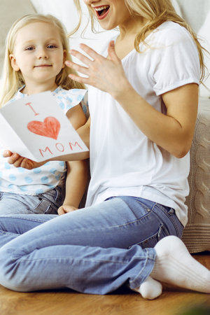 Happy mother day! Child daughter congratulates mom and gives her postcard with heart drawing. Family...