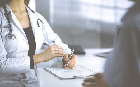 Unknown woman-doctor is prescribing some antibiotics for her patient, while they are sitting at the desk in the cabinet in a clinic. Female physician with a stethoscope is writing at clipboard, close-up. Perfect medical service in a hospital. Medicine concept.の写真素材