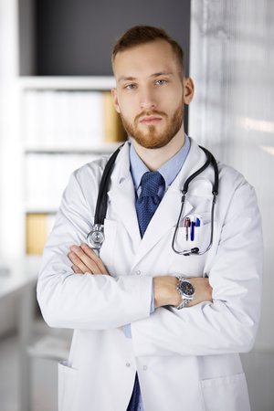 Red-bearded doctor standing straight in clinic near his working place. Portrait of physician. Medicine, healthcareの写真素材