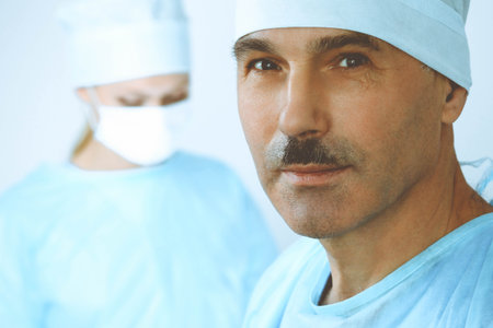 A male surgeon headshot, a group of surgeons is operating in the background. Health care conceptの写真素材