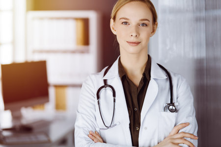 Cheerful smiling female doctor standing in clinic. Portrait of friendly physician woman. Medical service in hospital. Medicine conceptの写真素材